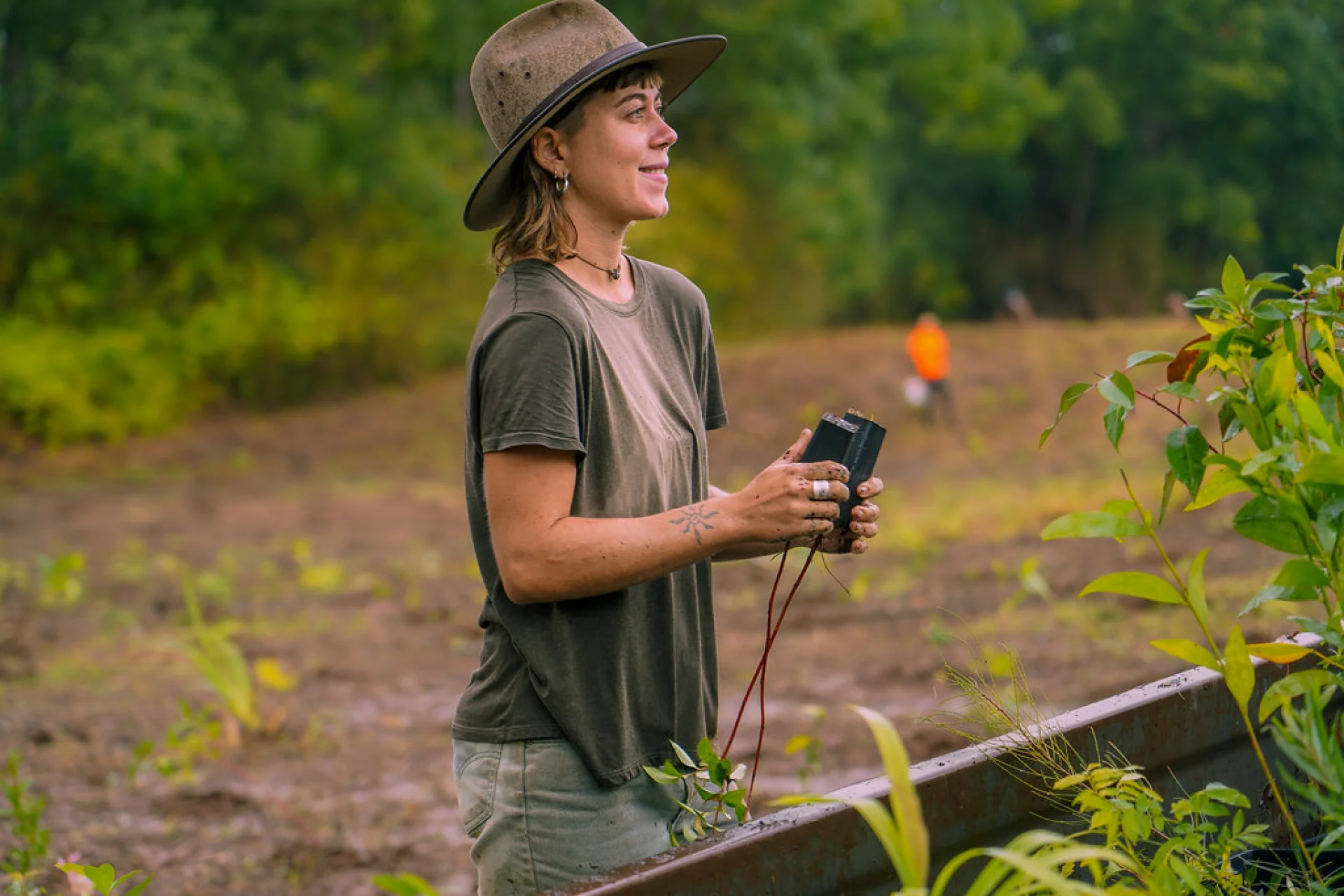 Volunteer Bonnie kneeling to plant a native tree seedling at Evertreen’s Queensland restoration site
